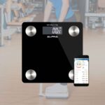 Black glass SRS475 BMI Bluetooth scale with the phone app showing body metrics