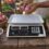 Price computing scale with an empty tray at a vegetable stall beside baskets of red onions